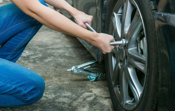 A Person change her flat tire on the road.